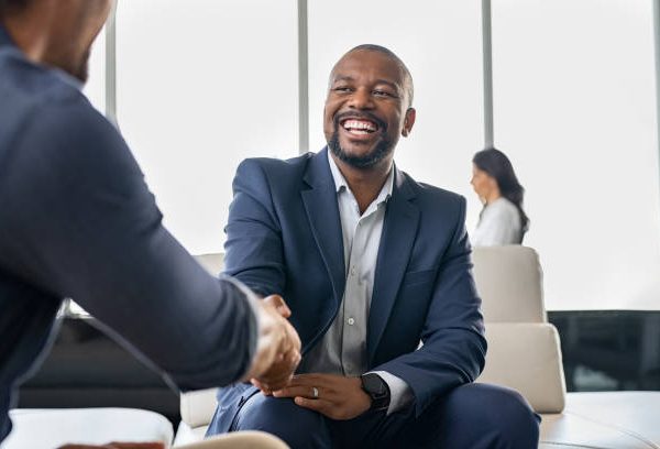 Two happy mature business men shaking hands in modern office. Successful african american businessman in formal clothing closing deal with handshake. Multiethnic businessmen shaking hands during a meeting.